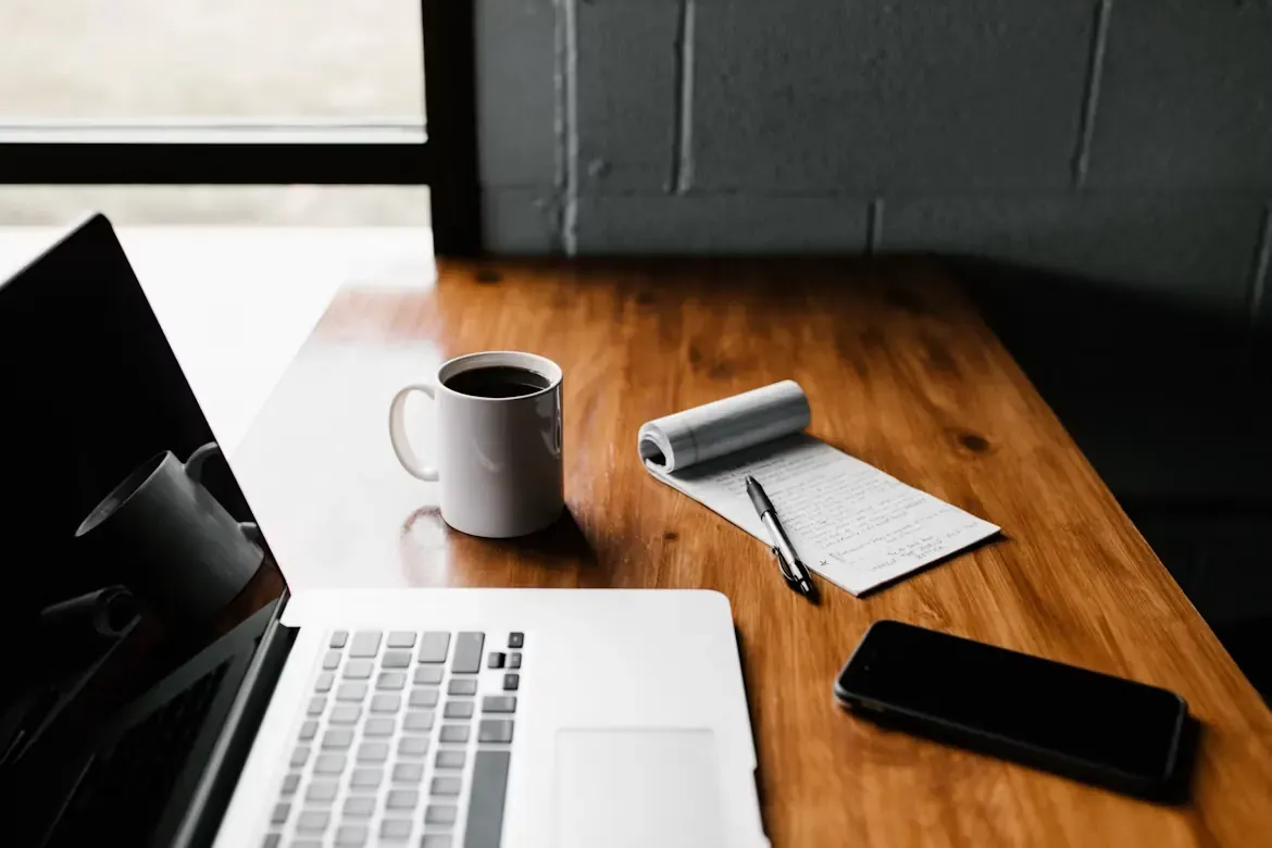 A laptop, coffee and handwritten notes on a wooden desk
