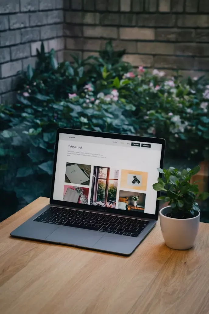 A laptop showing a website on a wooden table surrounded by plants